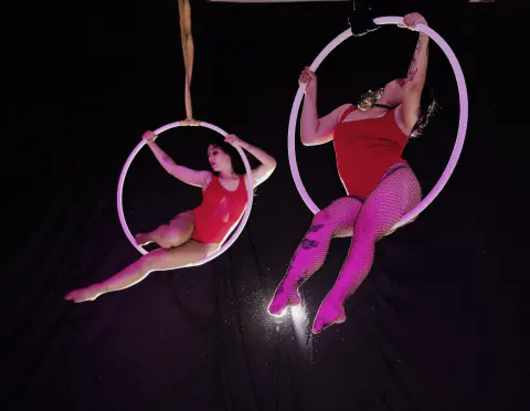 Dos acróbatas en aros aéreos con trajes rojo y rosado